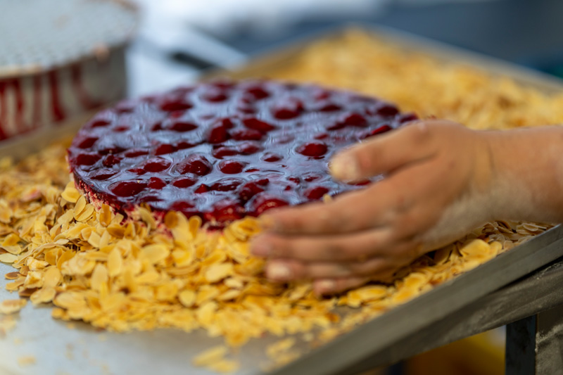 Blechkuchen wird in der Backstube von Hand mit Marmelade und Mandeln belegt